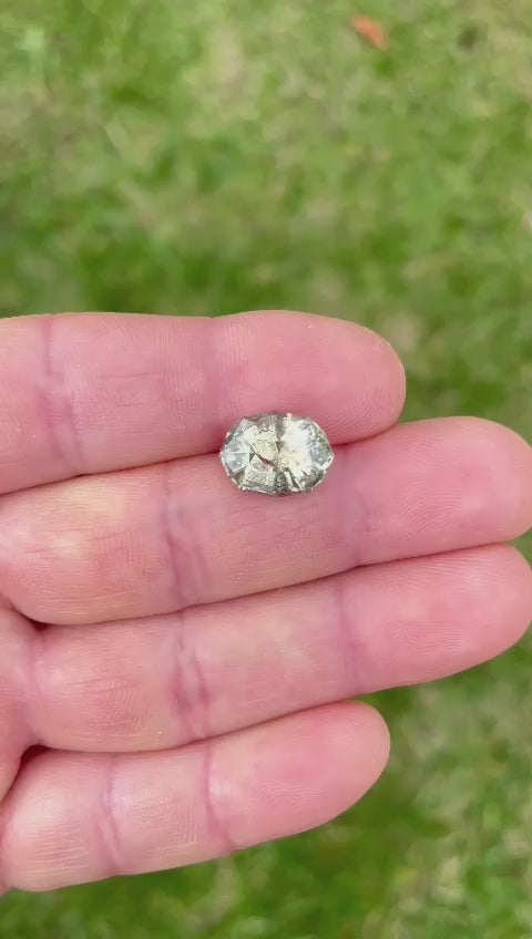 Detailed view of a color-changing sapphire being rotated in hand, showcasing the gemstone's clarity, cut, and natural color variations, emphasizing its origin and untreated quality.