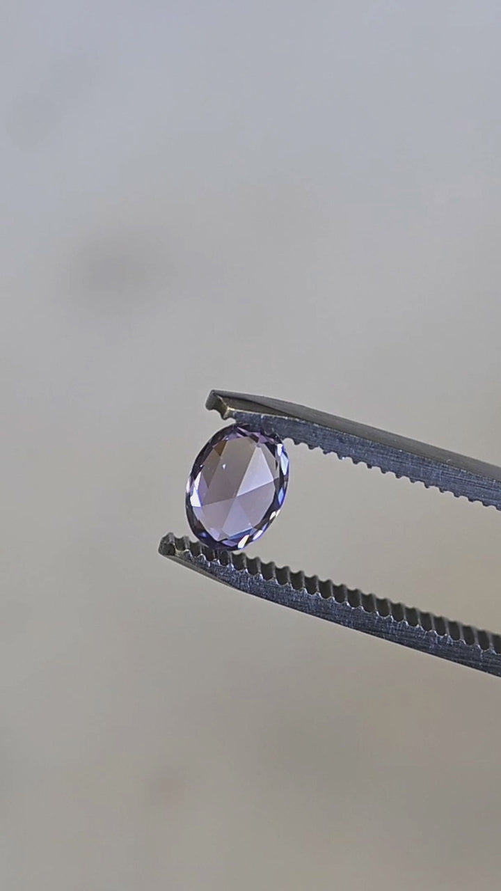 Natural Madagascar sapphire turning in tweezers, showcasing lavender, pink, and violet tones with excellent facet definition.