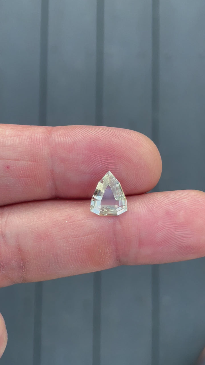 A 360-degree view of a 2.47-carat yellow-green sapphire in a modified geometric step cut. The video highlights the unique shield-like shape and brilliance of the untreated stone. The sapphire, sourced from Sri Lanka, has dimensions of 11.68mm by 9.62mm by 2.63mm.
