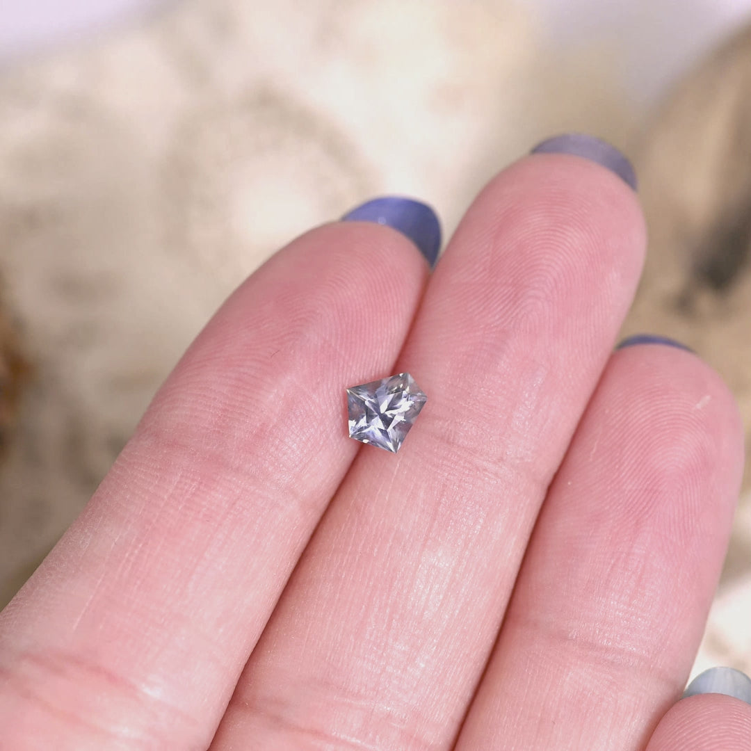 0.85 carat unheated Montana sapphire modified kite cut shown on hand, sparkling with blue green violet tones for bespoke engagement ring or custom jewelry.