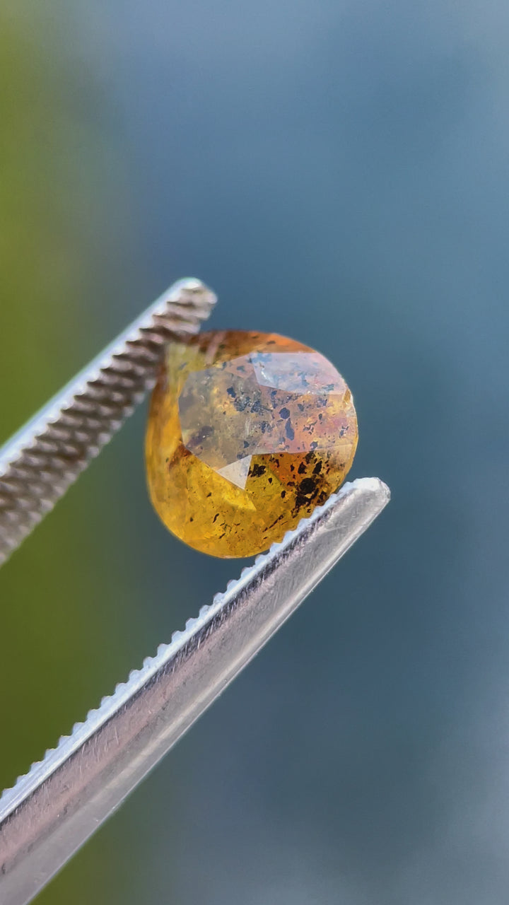 Rotating view of a pear-shaped 3.03-carat sapphire with yellow, orange, and black inclusions, capturing its luster and unique cut.