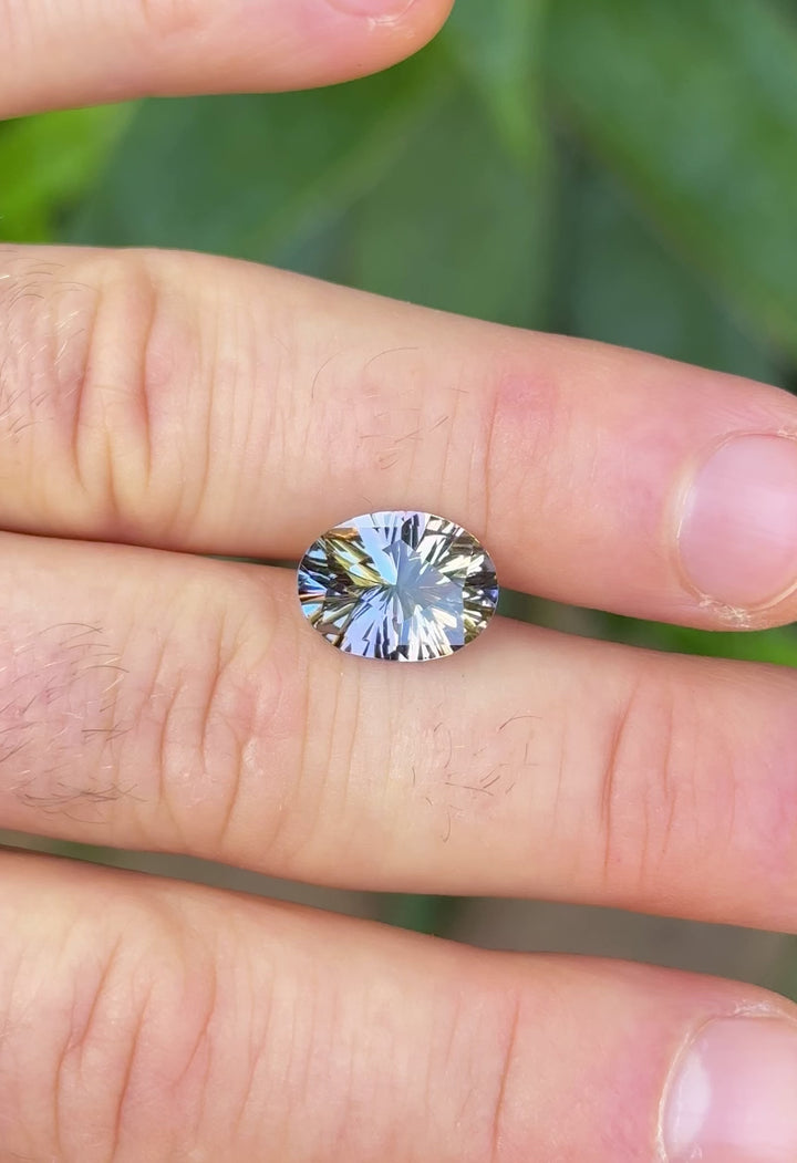 Natural light video of a 4.78-carat Tanzanite gemstone resting on fingers, showing brilliant flashes of green, lavender, and pastel hues from its precision oval concave cut