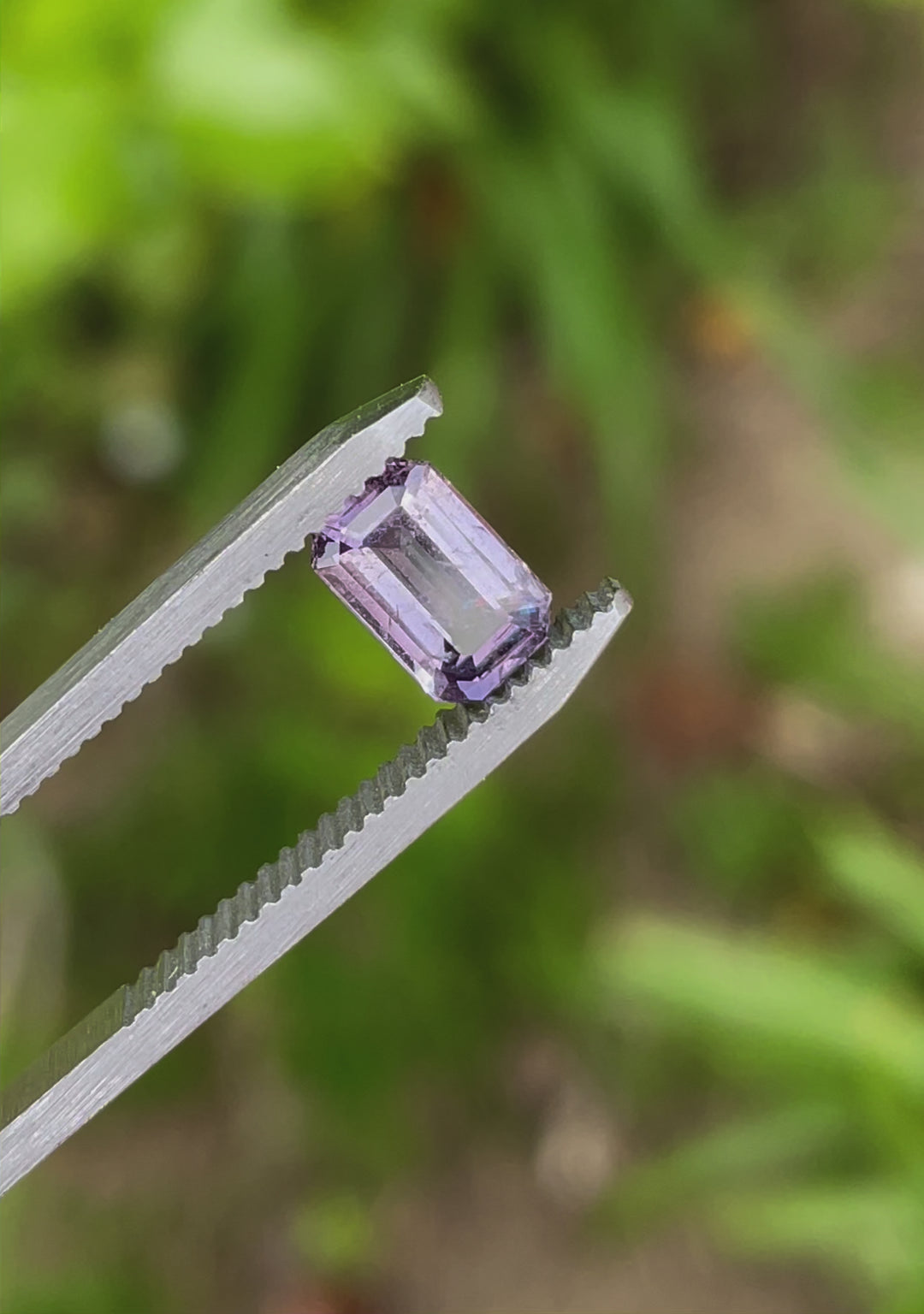 A video showcasing a 1.24-carat modified emerald-cut sapphire with a brown and purple hue. The gem reflects a play of light as it is gently rotated, highlighting its unique facets and clarity.