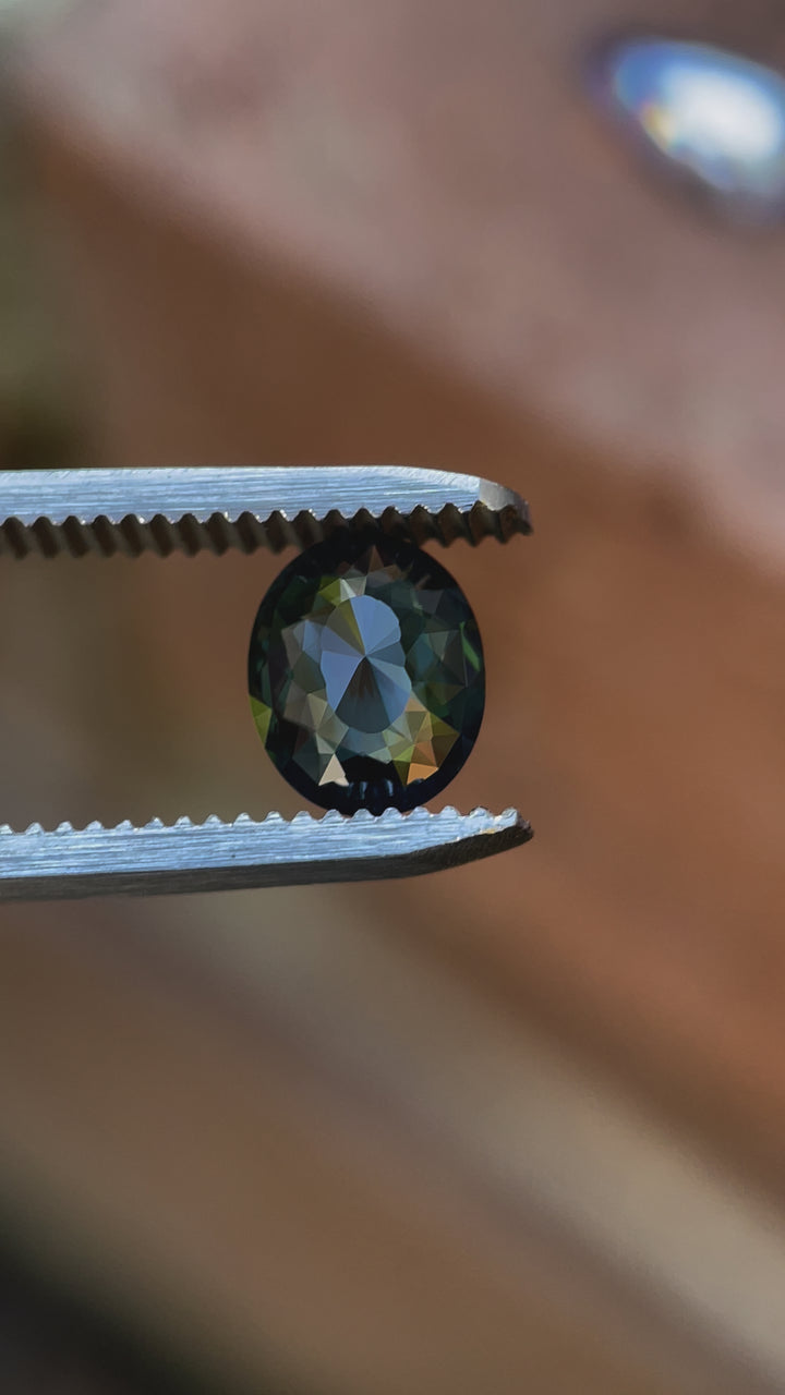 A close-up video focusing on the facets and vibrant colors of a 1.72-carat mix cut oval sapphire. The gemstone features green, blue, and teal hues, untreated and ethically sourced from Madagascar.