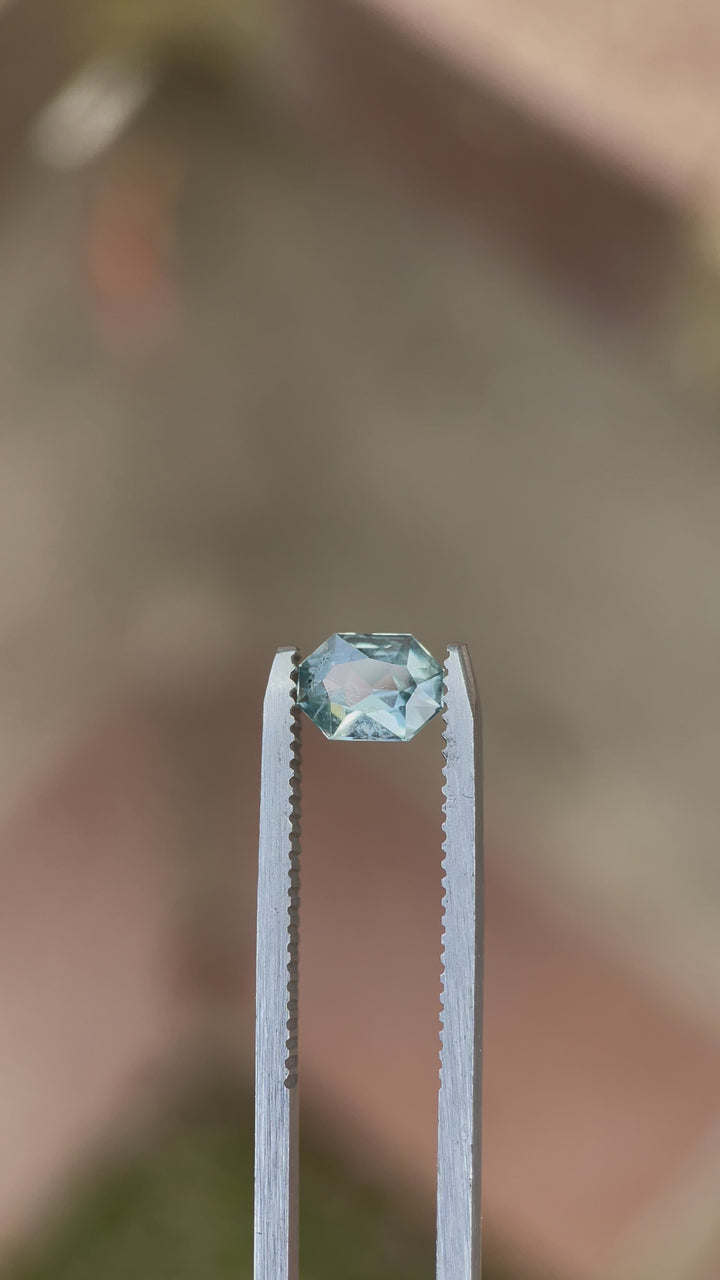 A video showcasing a custom octagonal radiant cut sapphire in yellow and seafoam colors, originating from the Umba River, Tanzania. The gemstone weighs 0.86 carats and exhibits stunning light reflection.