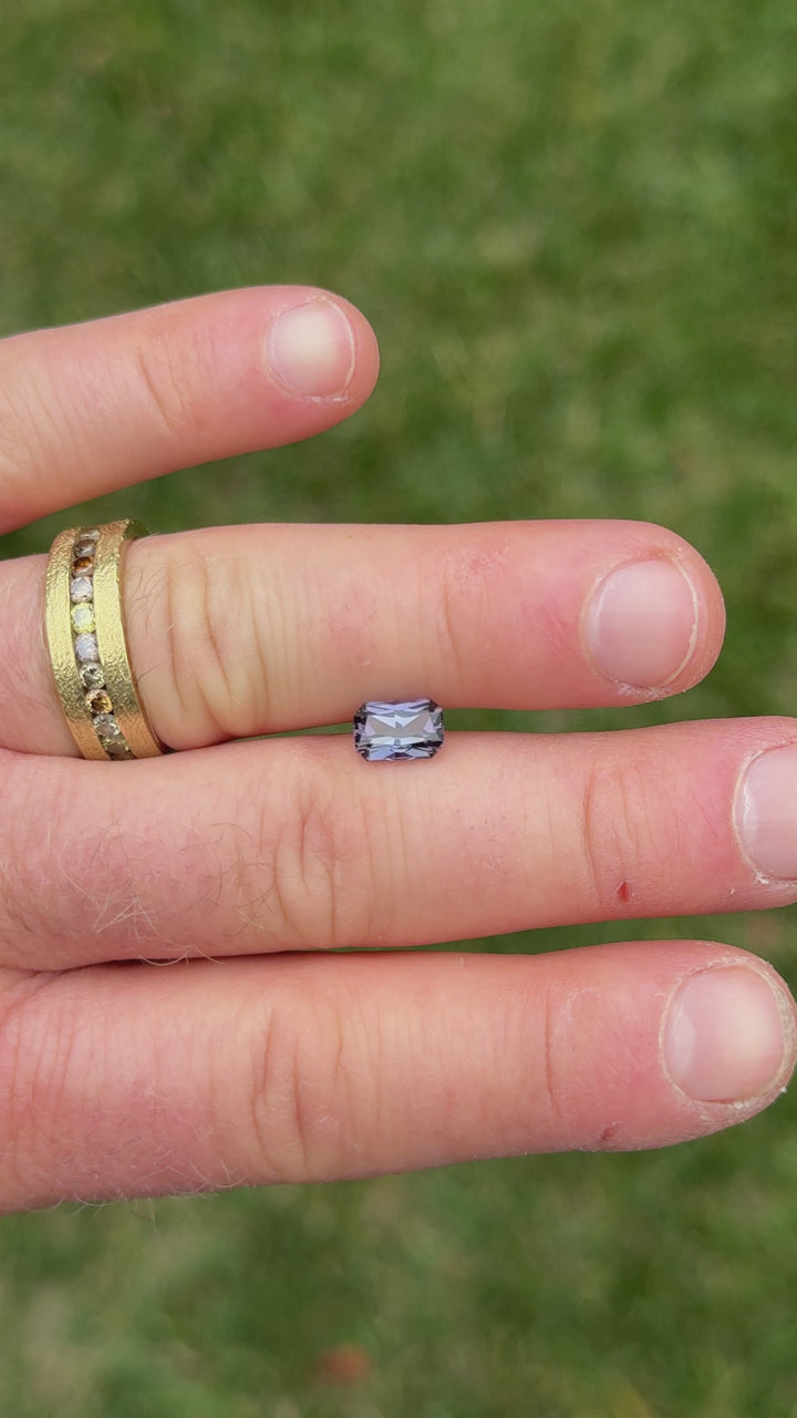 1.59CT antique radiant Tanzanite gemstone with vivid color flashes of green and violet, displayed between fingers for scale