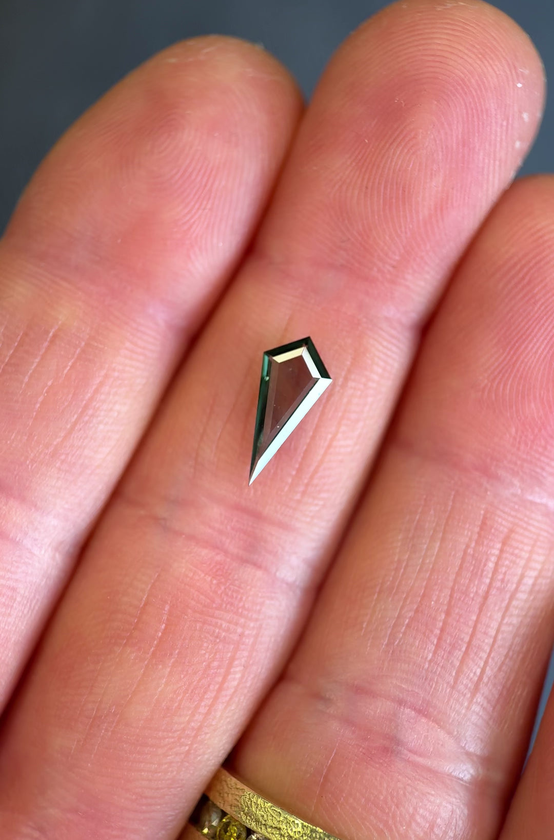 Hand-held teal green sapphire showing elongated kite portrait shape, color zoning, and light movement.