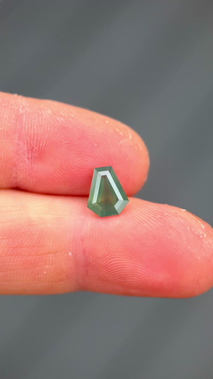 1.88ct opalescent teal blue green sapphire rotating in hand, revealing shifting oceanic tones and broad step-cut reflections.