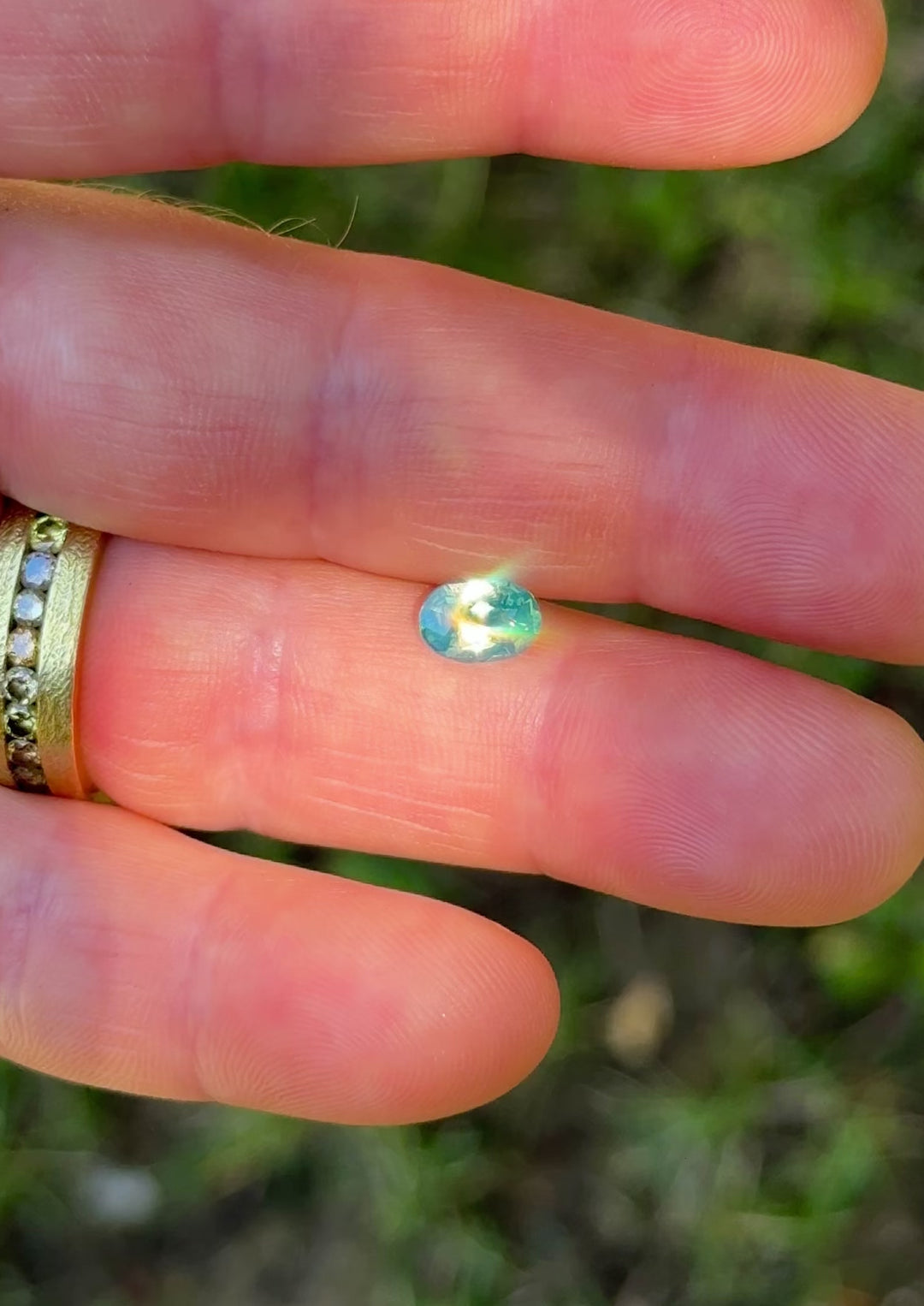 1.57ct opalescent teal blue green sapphire rotating in hand, revealing shifting oceanic tones and precision elongated oval brilliance.