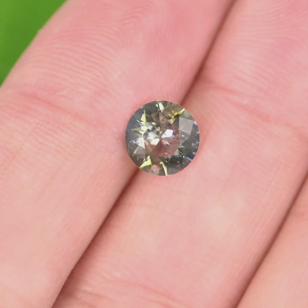 Close-up of 1.08 carat blue and brown tanzanite custom modified round brilliant resting on green leaf, displaying brilliance, symmetry, and precision faceting for fine custom jewelry.