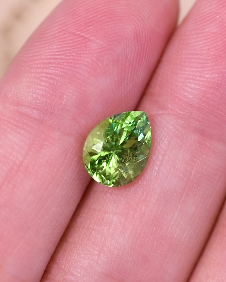Macro video of 2.85 carat Tsavorite garnet resting on surface, capturing light play, internal sparkle, and the dynamic color shifts of the modified brilliant pear cut, unheated Tsavorite from Kenya.