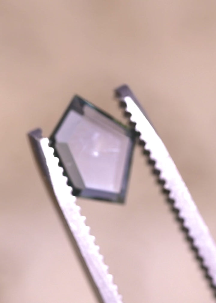 Close-up video of an untreated Montana sapphire held in tweezers, demonstrating color shift from teal blue seafoam to purple and the symmetry of the geometric pentagon portrait cut.