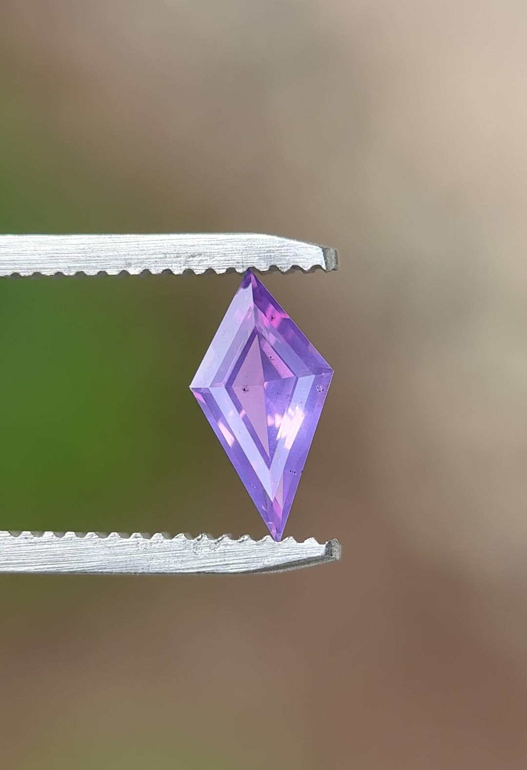 Natural loose sapphire rotating in gem tweezers showing off precision kite cut faceting and vibrant pink and purple hues