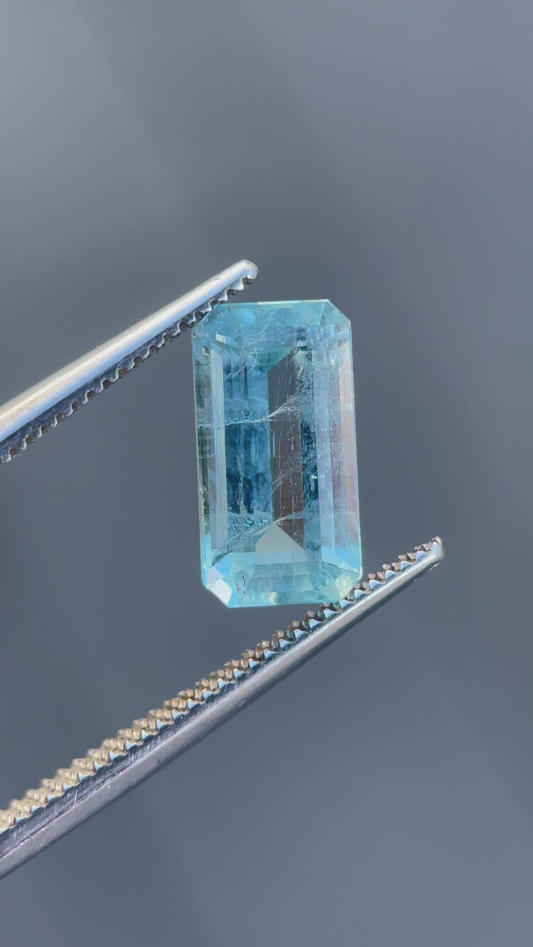 A mesmerizing video of an emerald-cut aquamarine gemstone held in precision tweezers, rotating gently to showcase its mint blue hue, sparkling facets, and exceptional clarity.