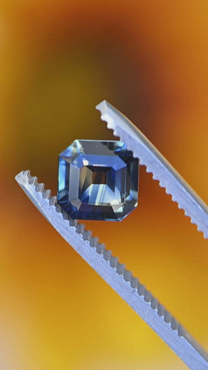 Loose Madagascar parti sapphire Asscher cut rotating in tweezers to display color zoning and brilliance