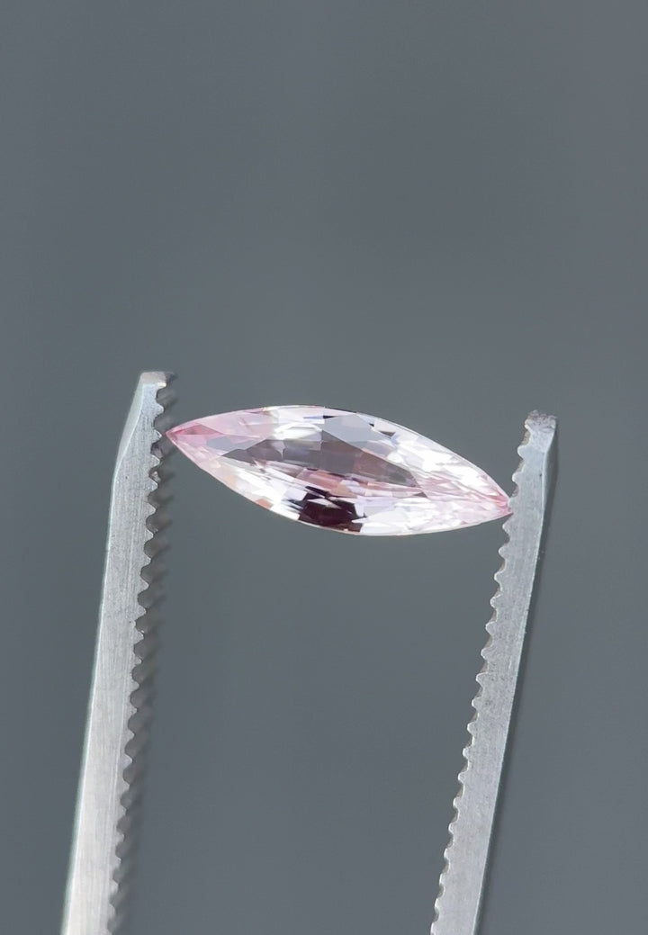 Video of 1.03CT blush pink sapphire rotating in gemstone tweezers, showcasing its brilliance, color depth, and reflections from the precision marquise mixed cut, heated sapphire from Sakaraha, Madagascar.