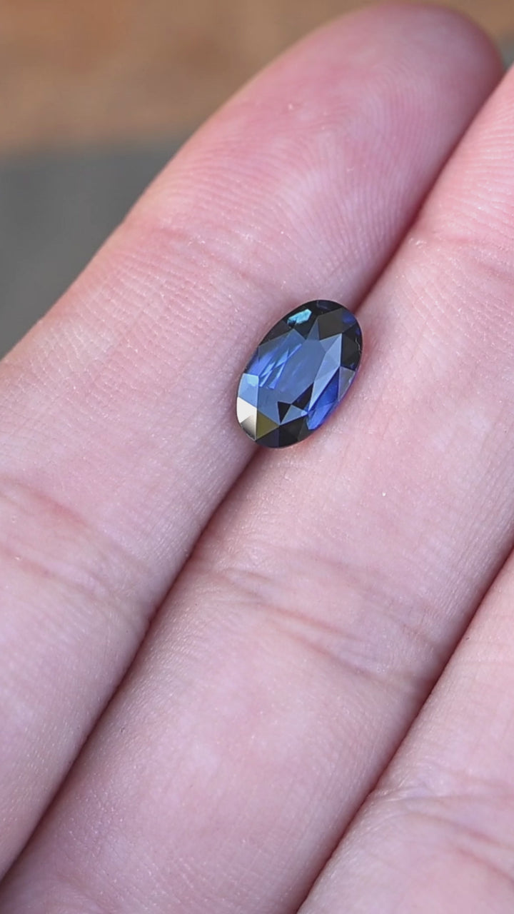 2.02ct deep blue elongated moval cut sapphire from madagascar rotating on fingertips under natural lighting.