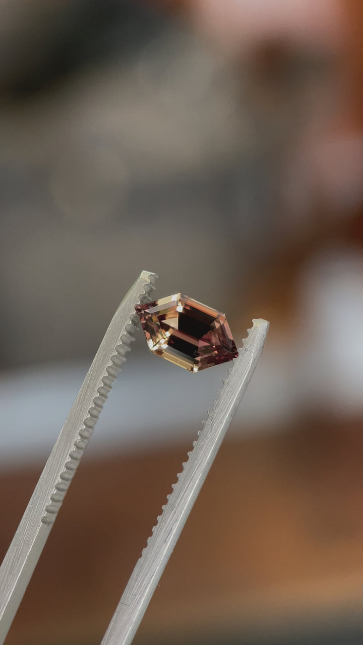 A rotating video of a 1.22-carat Songea sapphire, showcasing its intricate hexagon step cut and vibrant mix of brown, orange, and pink hues in natural lighting.