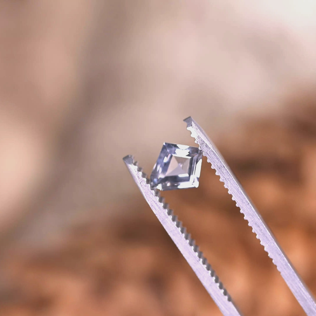 Close-up tweezers video of 0.98 carat unheated Montana sapphire, gray violet teal tones shifting as the custom kite step cut catches the light
