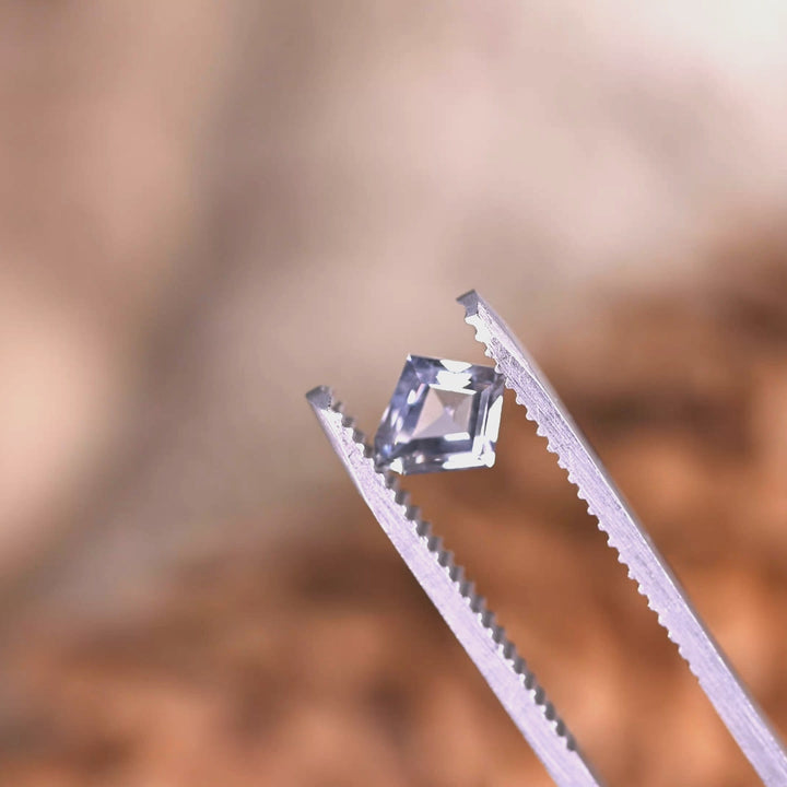 Close-up tweezers video of 0.98 carat unheated Montana sapphire, gray violet teal tones shifting as the custom kite step cut catches the light