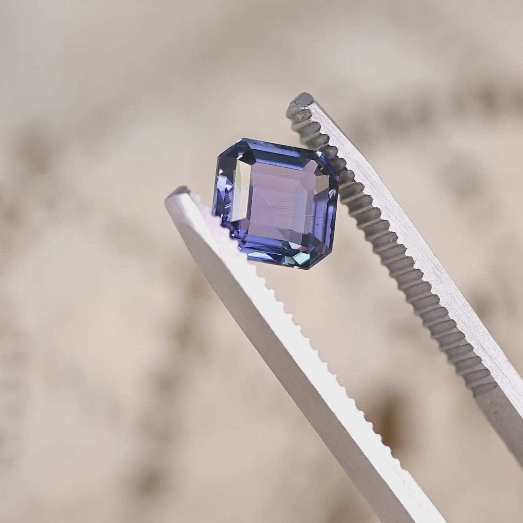 Close-up video of 1.93ct blue violet Tanzanite Asscher cut held in tweezers, square step cut gemstone from Tanzania displaying sharp facet reflections and vivid violet blue tones