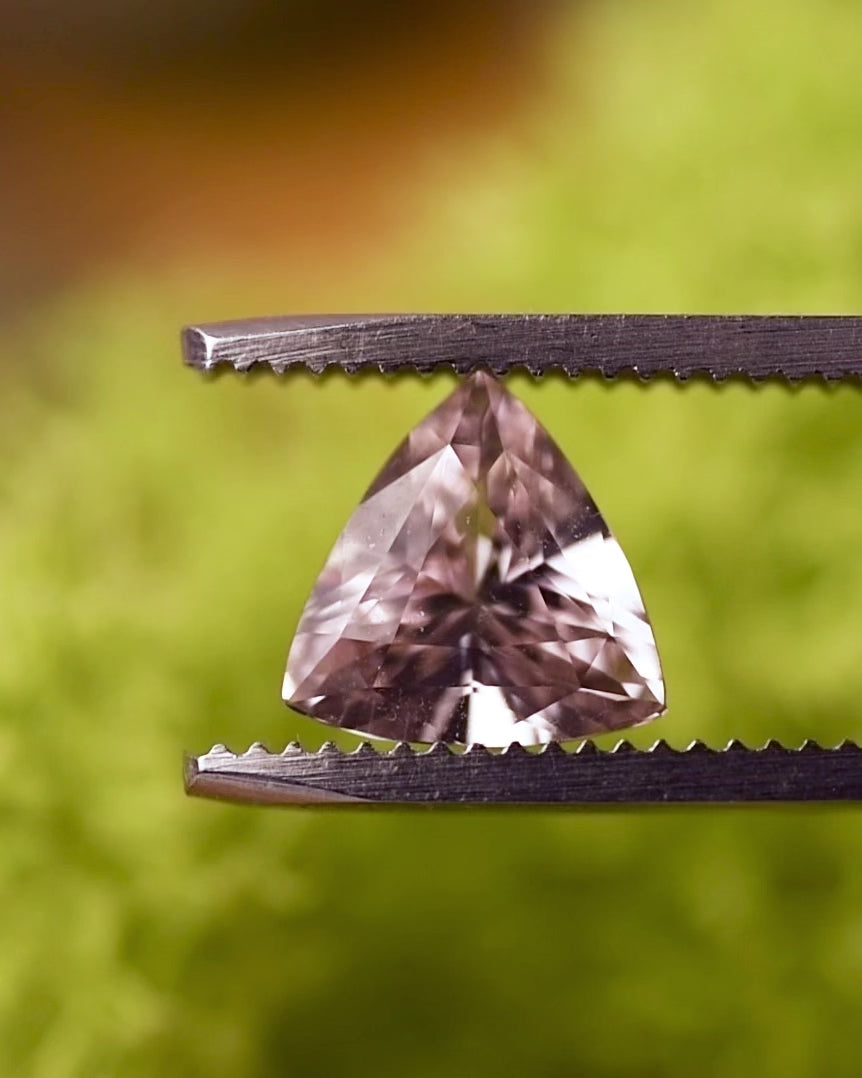 Video of 2.06CT pink and peach sapphire rotating in gemstone tweezers under natural light, highlighting brilliance, transparency, and fire of the trillion cut, untreated sapphire from Sakaraha, Madagascar.