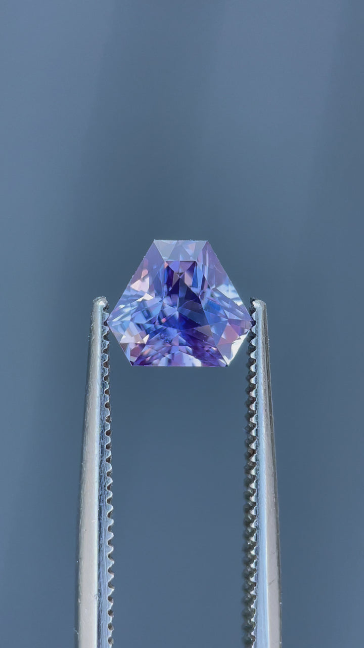 A stunning 1.56-carat lavender sapphire with a custom mix brilliant triangle cut, showcasing its natural brilliance and color shift under different lighting conditions. Ethically sourced from Sri Lanka, this untreated gemstone exhibits shades of purple, pink, and lavender.