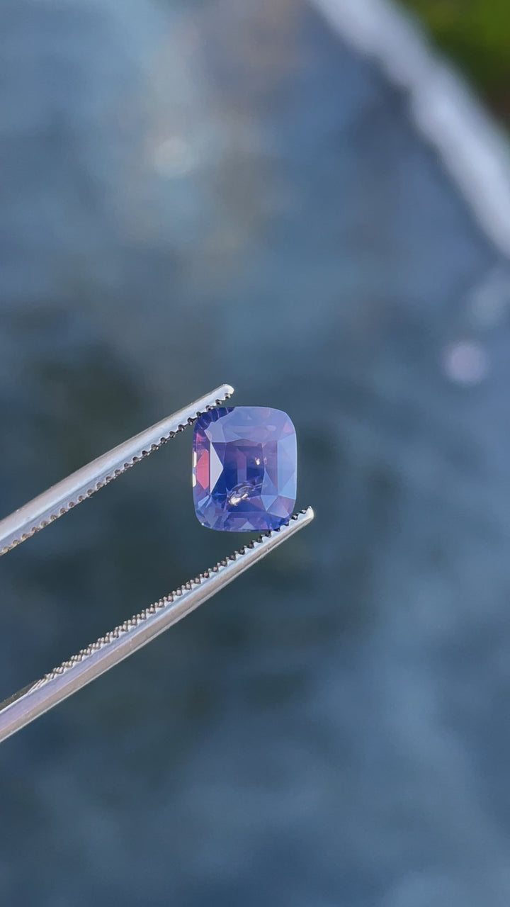 Video of a 2.56-carat cushion-cut sapphire with mauve, pink, and purple tones, captured under natural lighting.