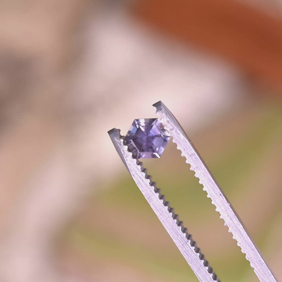 Close-up video of 0.42ct purple pink Montana sapphire held in tweezers, precision hexagon step cut gemstone from Montana USA displaying sharp edges and mirrored step faceting