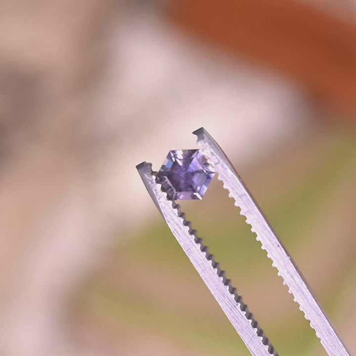 Close-up video of 0.42ct purple pink Montana sapphire held in tweezers, precision hexagon step cut gemstone from Montana USA displaying sharp edges and mirrored step faceting