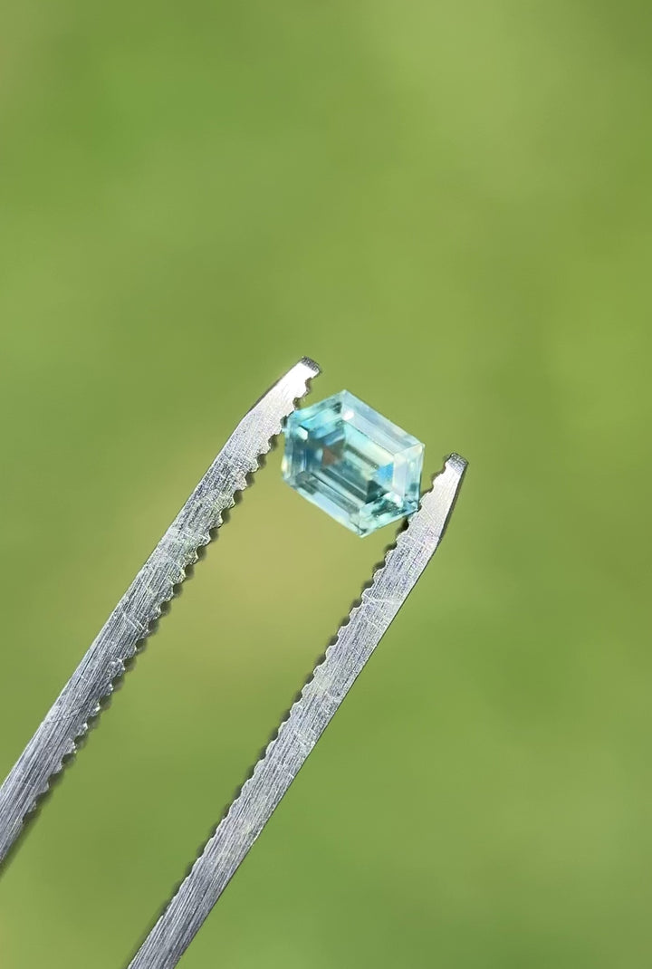 Video of 0.83 carat Montana sapphire in step cut hexagon shape, rotating to show teal, blue, and yellow parti colors in daylight