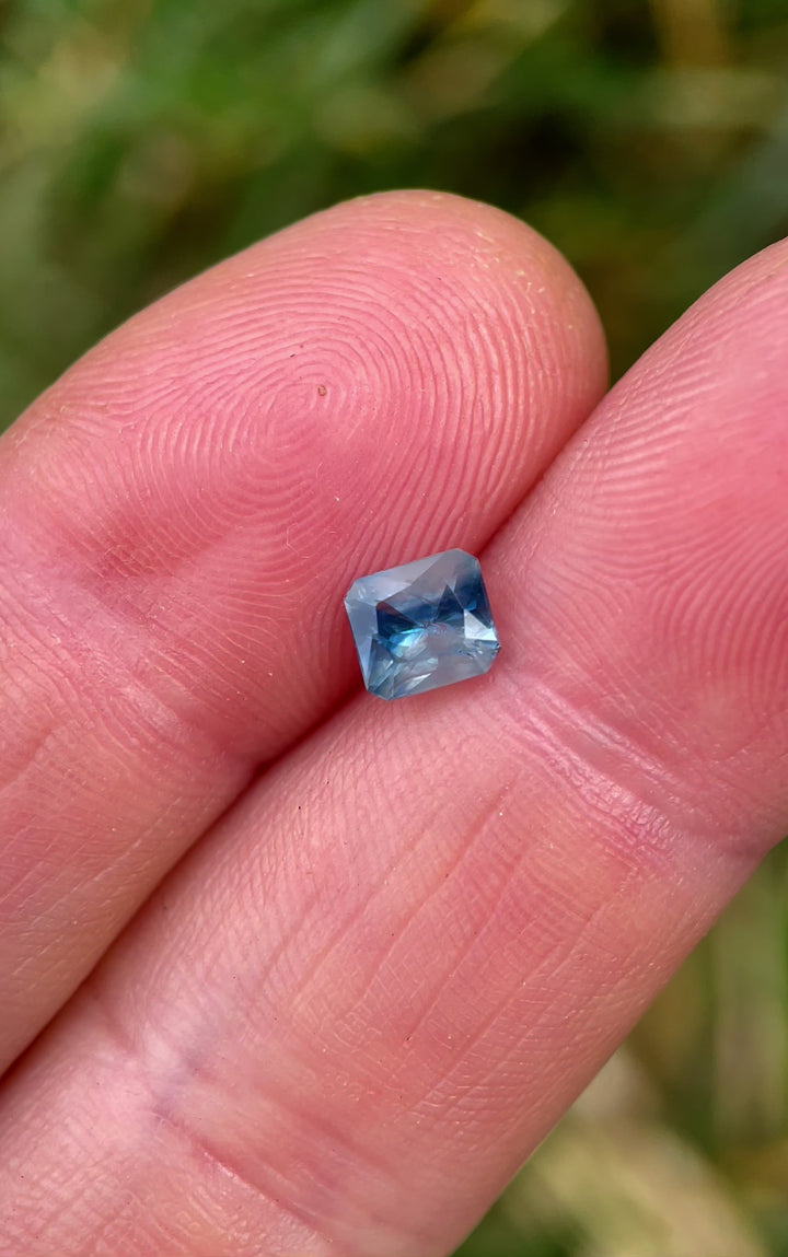 A rotating video of a Parti Blue and White Sapphire gemstone with a Mixed Radiant Cut, weighing 1.03 carats, displaying its intricate facets and color interplay under natural light.