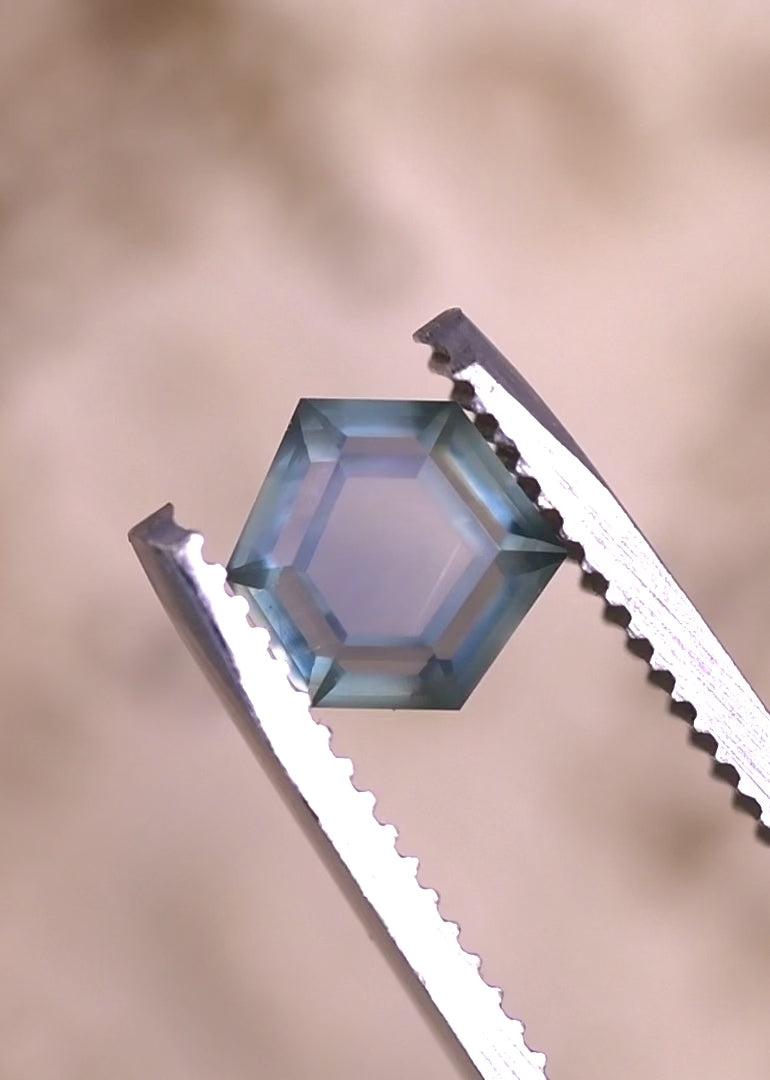 Video of a 1.37 carat teal blue seafoam Montana sapphire rotating in tweezers, revealing geometric hexagonal step cut facets, natural color zoning, and untreated sapphire brilliance under shifting light.
