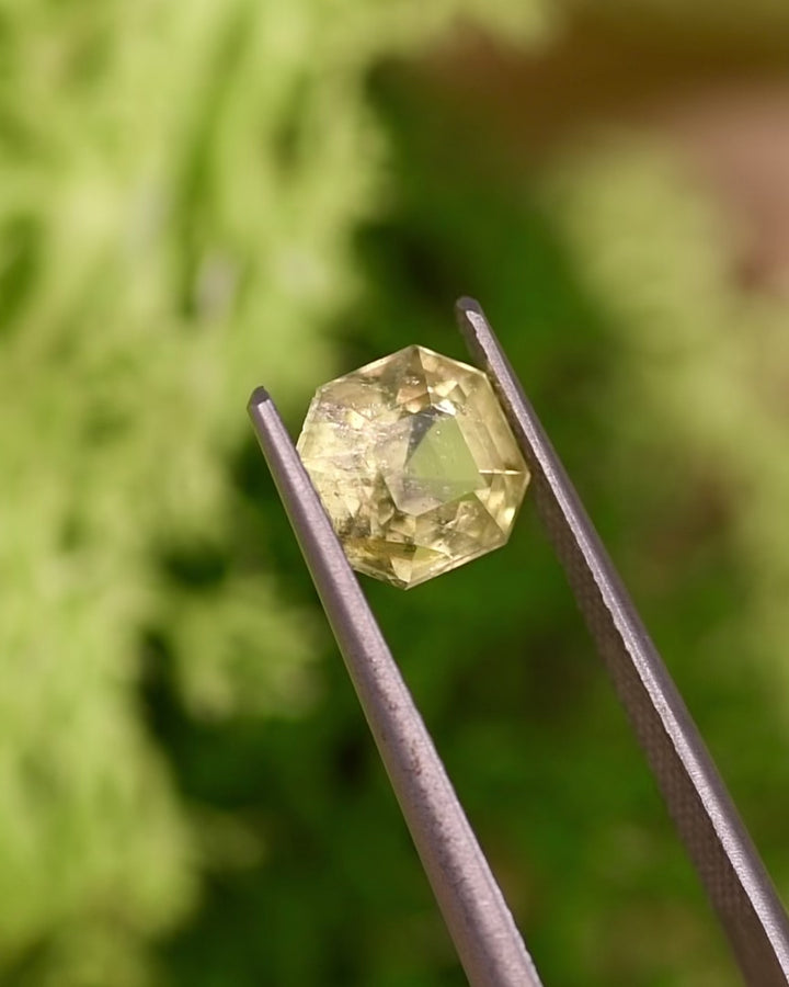 Video of 1.88CT teal yellow sapphire rotating in tweezers under natural light, displaying the Asscher cut’s step facets, teal-yellow tones, and internal brilliance of this unheated gemstone from Umba River Valley, Tanzania.
