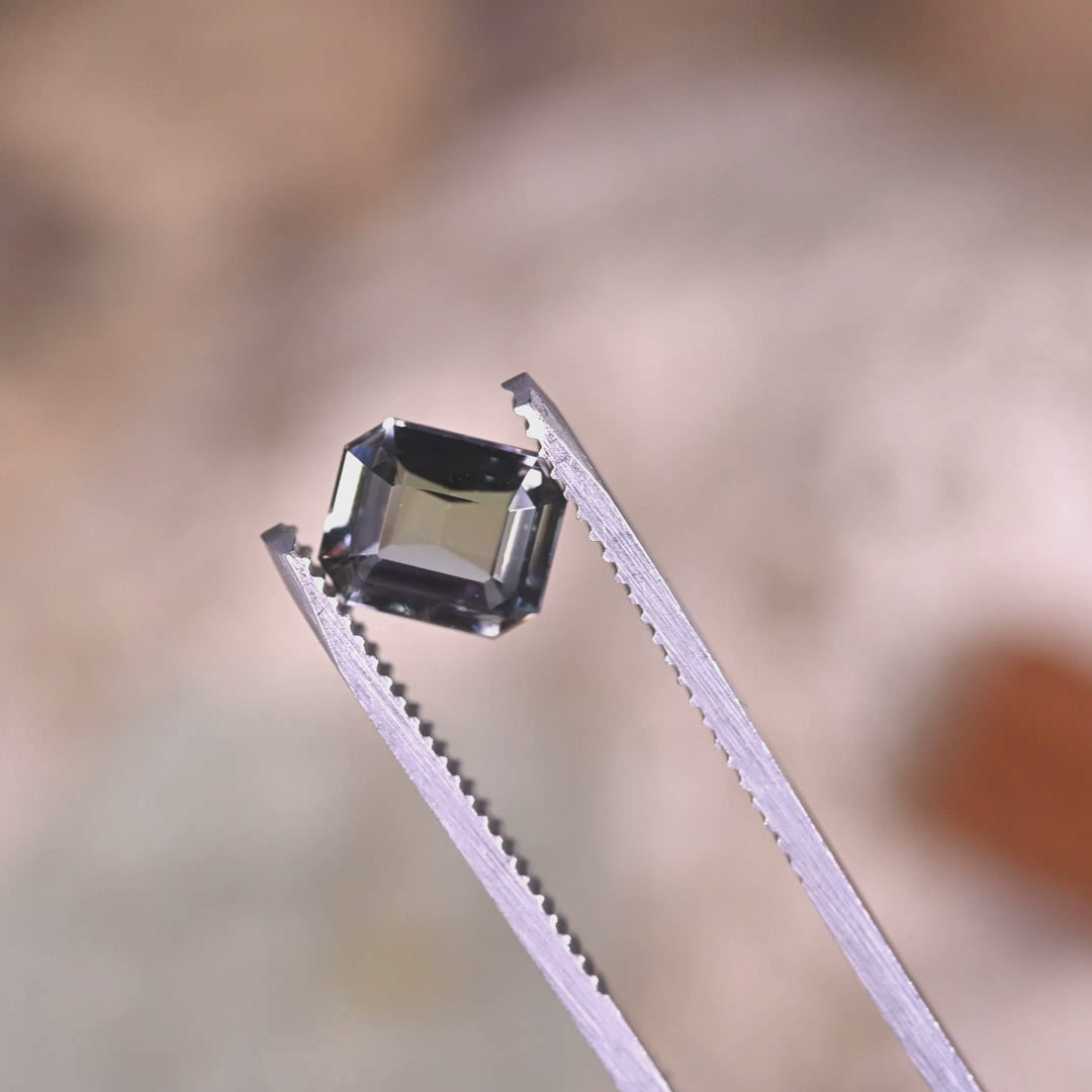 Close-up video of 1.67ct teal blue green Tanzanite modified emerald cut held in tweezers, custom precision cut gemstone from Tanzania displaying crisp beveled corners and dynamic light performance