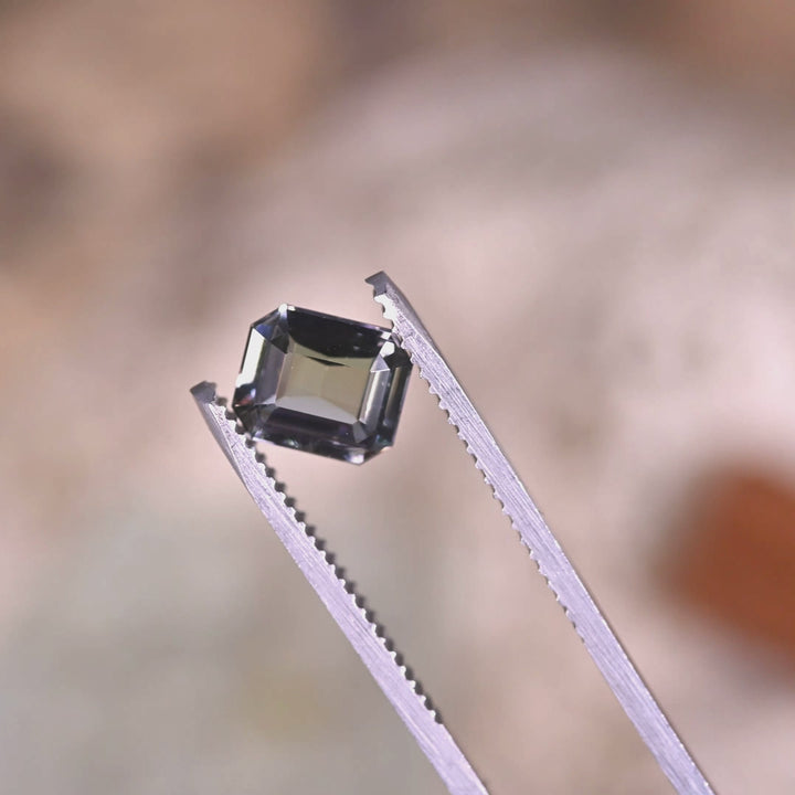 Close-up video of 1.67ct teal blue green Tanzanite modified emerald cut held in tweezers, custom precision cut gemstone from Tanzania displaying crisp beveled corners and dynamic light performance