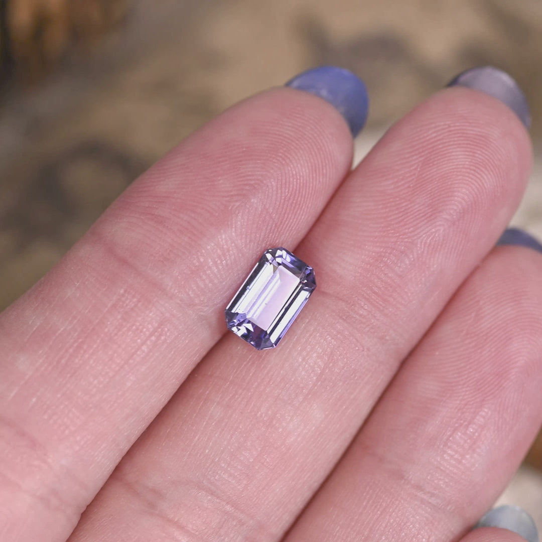 2.08 carat lavender purple Tanzanite octagonal step cut rotating on hand under natural light, untreated Merelani Hills gemstone showing mirrored step reflections and vivid violet blue color shift for custom jewelry