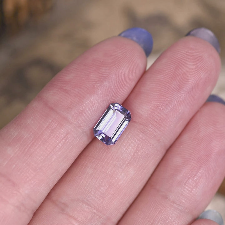 2.08 carat lavender purple Tanzanite octagonal step cut rotating on hand under natural light, untreated Merelani Hills gemstone showing mirrored step reflections and vivid violet blue color shift for custom jewelry