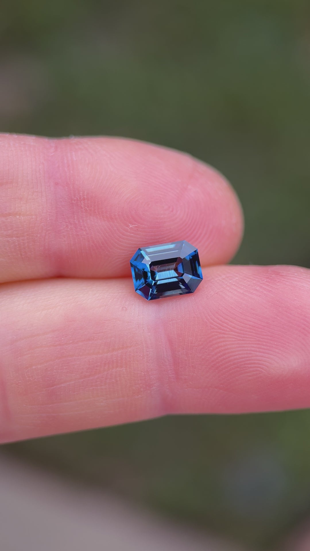 Teal indigo sapphire rotating under natural light showing step cut reflections and strong color saturation.