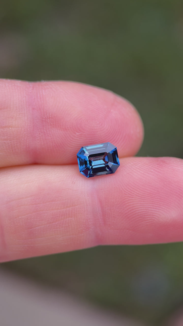 Teal indigo sapphire rotating under natural light showing step cut reflections and strong color saturation.
