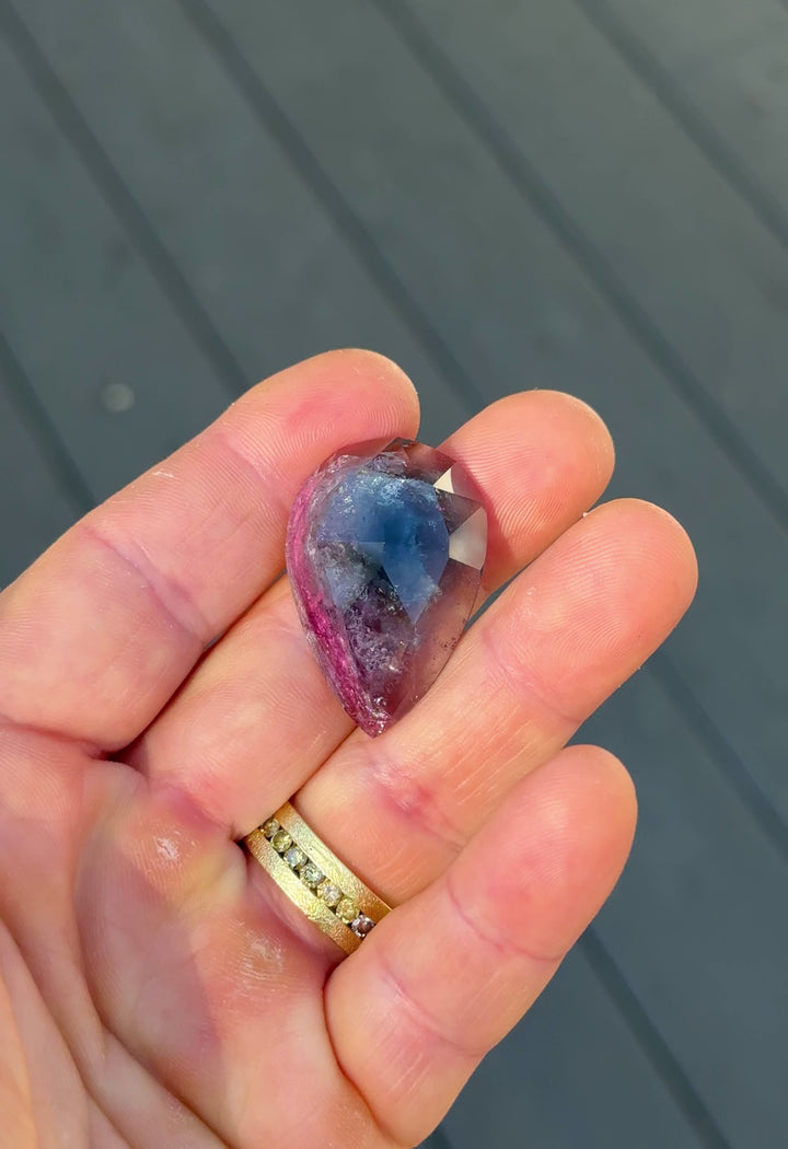 Handheld video of untreated 46.80CT tourmaline gemstone displaying its vivid blue, pink, and purple hues as it moves through natural light, custom pear rose cut from Afghanistan.