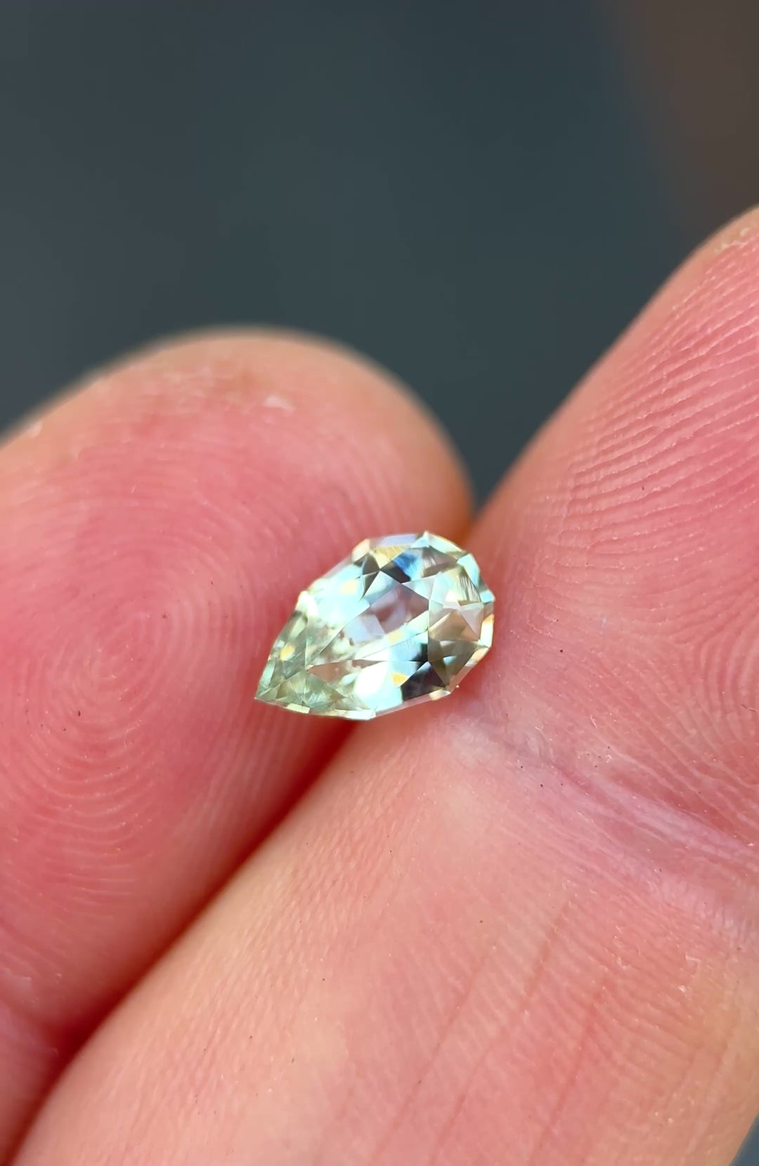 1.24ct light seafoam green sapphire rotating in hand, revealing soft aqua and mint flashes across the precision pear cut.