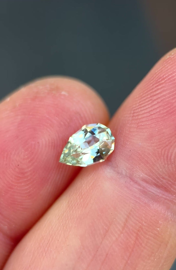 1.24ct light seafoam green sapphire rotating in hand, revealing soft aqua and mint flashes across the precision pear cut.