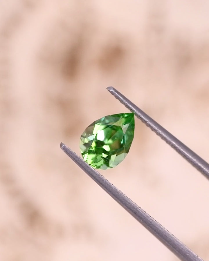 Video of 1.39CT tsavorite garnet rotating in gemstone tweezers, capturing vibrant electric lime green flashes and brilliance of the pear cut, untreated gem from Kenya.