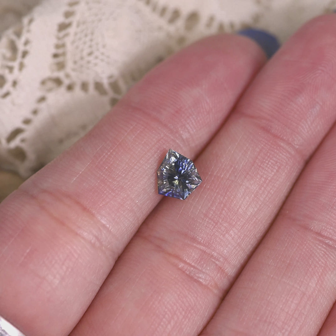 Loose blue and colorless sapphire from Madagascar rotating under light displaying the geometric shield shape and bright concave facets.