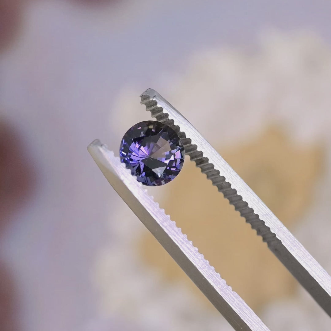 Close-up video of 1.19ct orange purple Tanzanite round brilliant held in tweezers, precision faceted untreated gemstone from Tanzania displaying clarity and vibrant bi color brilliance