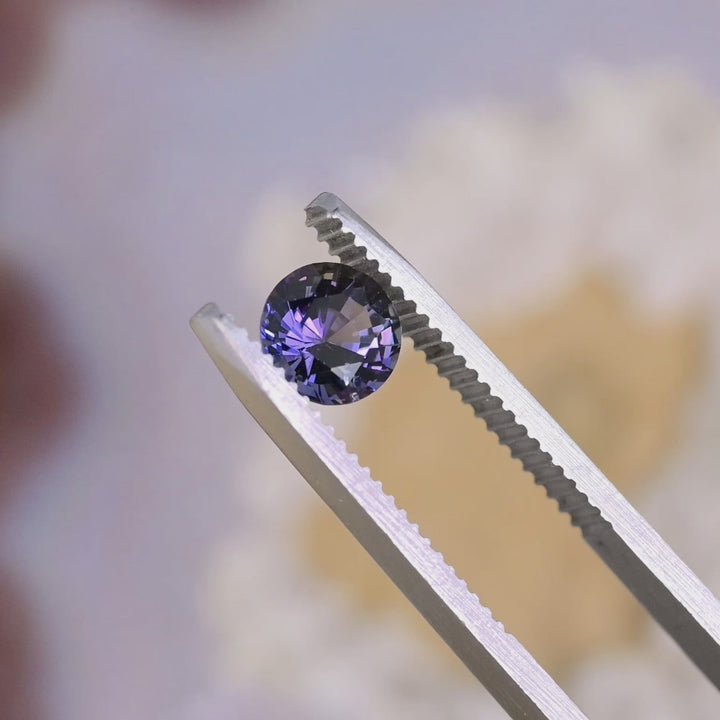 Close-up video of 1.19ct orange purple Tanzanite round brilliant held in tweezers, precision faceted untreated gemstone from Tanzania displaying clarity and vibrant bi color brilliance