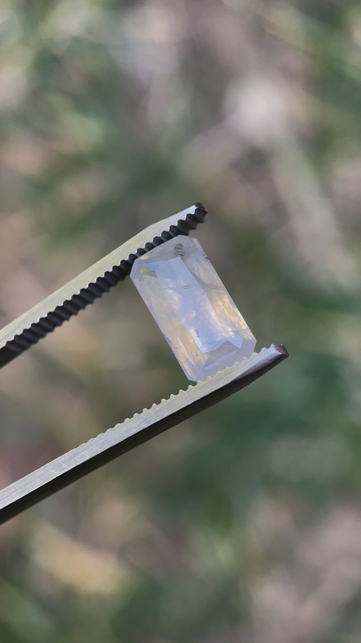 Detailed video of a radiant cut sapphire, weighing 4.18 carats, displaying opalescent white and yellow tones with intricate inclusions.