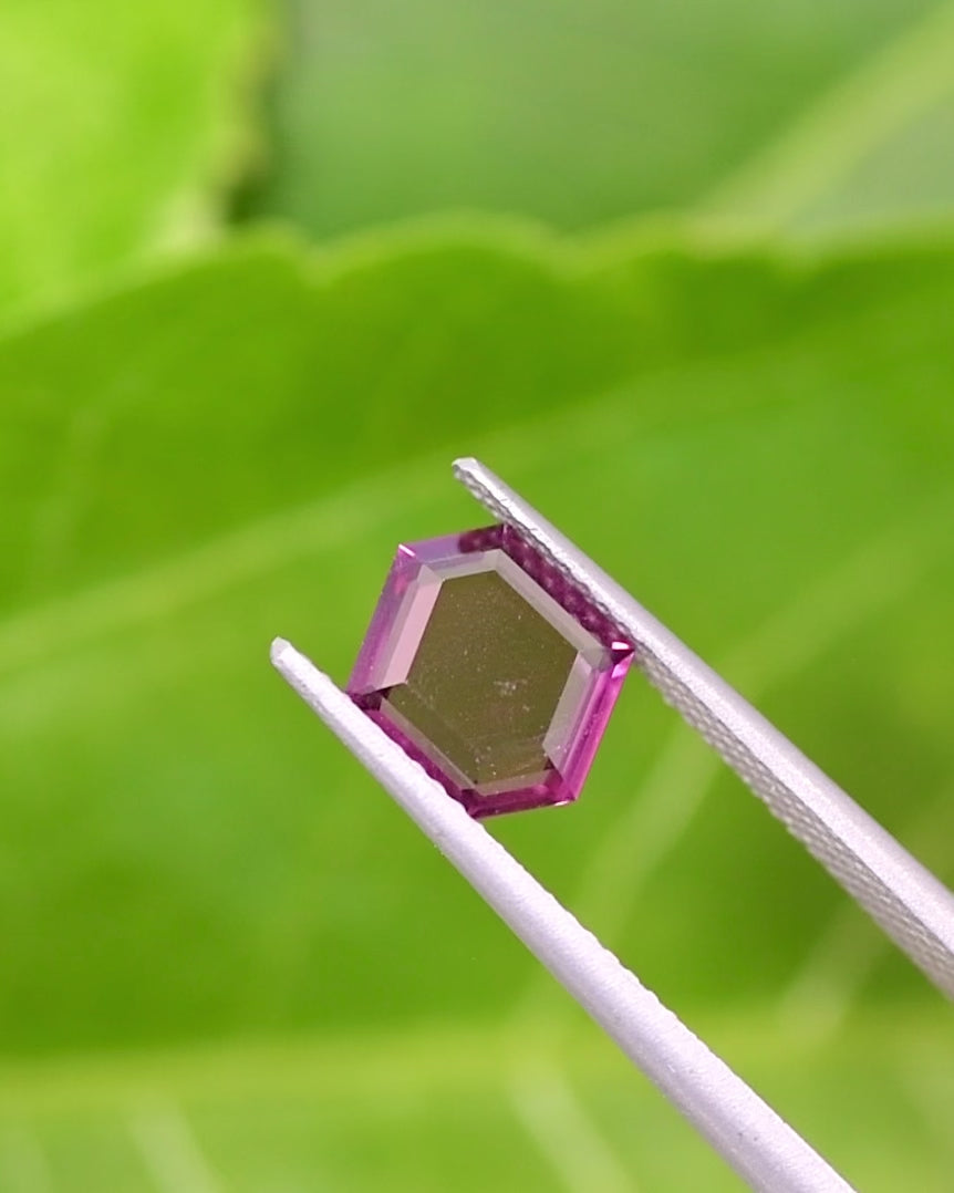Video of 1.71CT pink and purple garnet rotating in gemstone tweezers under daylight, showing facets, brilliance, and color transitions of the custom geometric step cut tablet, untreated garnet from Kenya.