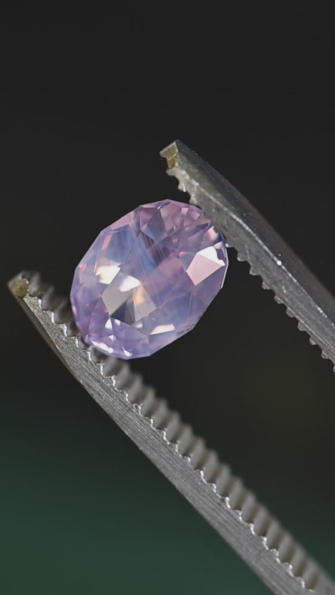 Loose opalescent pink sapphire turning in tweezers under natural light, revealing soft violet flashes and balanced oval symmetry from Sri Lanka.